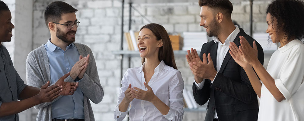 Group of workers recognizing an individual employee while standing in a circle and clapping.